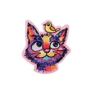 Könnte beinhalten: Gestickter Aufnäher mit einer bunten Katze und einem gelben Vogel auf dem Kopf. Das Gesicht der Katze ist eine Mischung aus Lila, Blau, Gelb und Rot. Der Aufnäher hat einen rosa Rand und ist für Kleidung oder Accessoires geeignet.