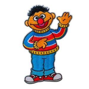 Può includere: Toppa ricamata raffigurante un personaggio dei cartoni animati con la pelle arancione, i capelli neri e il naso rosso. Il personaggio indossa un maglione a righe blu, rosse e gialle, pantaloni blu e scarpe rosse. Il personaggio saluta con un'espressione amichevole.