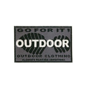 Könnte beinhalten: Ein rechteckiger grauer Patch mit schwarzem Text, der "GO FOR IT! OUTDOOR OUTDOOR CLOTHING ULTIMATE WEATHER CONDITIONS" lautet. Der Text ist von einem schwarz-weißen grafischen Design umgeben.