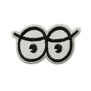 Könnte beinhalten: Ein weißer gestickter Aufnäher mit zwei schwarzen Augen. Die Augen sind schwarz umrandet und haben eine schwarze Pupille.