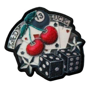 Könnte beinhalten: Ein gestickter Patch in Schwarzweiß mit einer roten Kirsche, einer schwarzen Billardkugel mit der Nummer 13, Spielkarten, Würfeln und einem Stern. Der Patch zeigt "Lucky" und "The Devil".