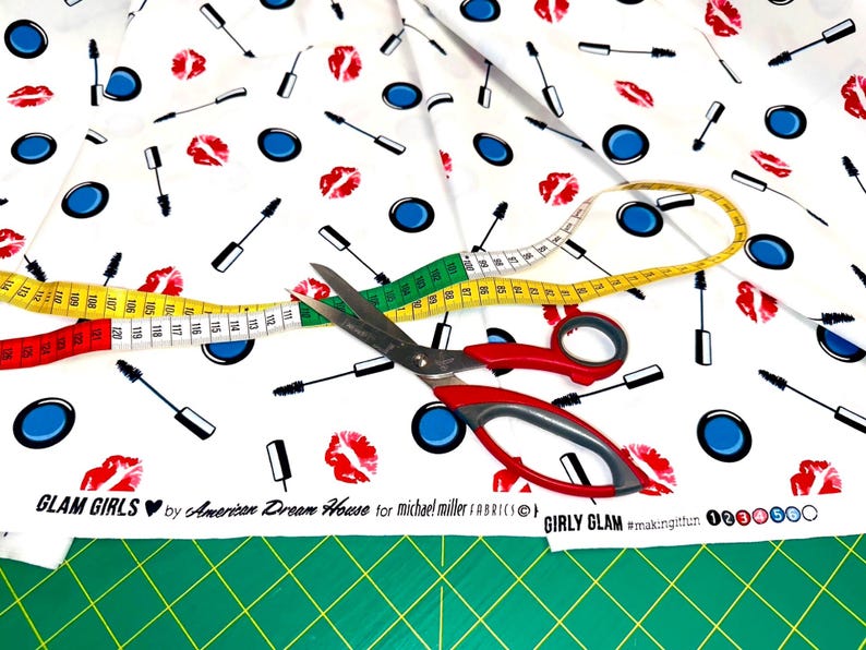 Nahaufnahme eines Kosmetik-Motivstoffs mit Lippen, Mascara, Pinseln und Lidschatten auf weißem Grund.