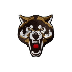 Pode incluir: Um emblema bordado apresentando a cabeça de um lobo rosnando com a boca aberta. O design utiliza fios castanho-escuros, bronzeados, brancos e pretos, com uma língua vermelha brilhante visível dentro da boca. O emblema tem uma borda preta.