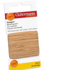 Puede incluir: Una bobina de hilo para zurcir Stopfgarn beige Gütermann Creativ. La etiqueta dice "100% Baumwolle/100% Cotton/100% Cotone" y "20 m 22 yds/vgs".