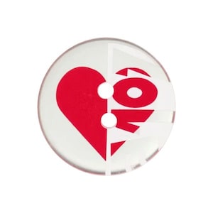 Peut inclure: Un bouton blanc avec un cœur rouge et le mot "LOVE" imprimé dessus. Le cœur est partiellement découpé, révélant le mot "LOVE" en dessous.