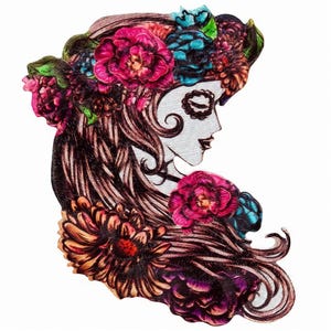 Könnte beinhalten: Ein gestickter Aufnäher mit dem Profil eines Gesichts mit Totenkopf-Make-up, langem braunem Haar und einem leuchtenden Blumenkranz. Das Design verwendet rosa, violette, blaue und orangefarbene Fäden, um detaillierte Blütenblätter zu bilden.