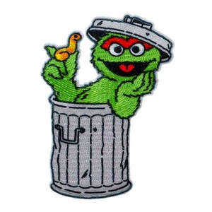 Può includere: Toppa ricamata con Oscar il brontolone di Sesame Street, che esce da un bidone della spazzatura grigio. Oscar è verde con sopracciglia rosse e bocca rossa, che tiene in mano un uccello giallo. Il bidone ha un coperchio argentato.