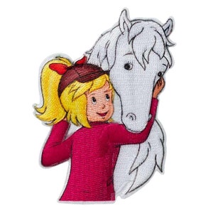 Op de afbeelding: Een geborduurde patch met een meisje met blond haar dat een rood shirt en een bruine hoed draagt, en een wit paard knuffelt.
