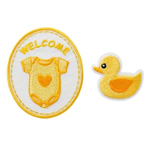 Könnte beinhalten: Zwei gelbe gestickte Bügelbilder. Ein Patch ist rund und sagt "WELCOME" mit einem Baby-Strampler darin. Der andere Patch ist eine gelbe Gummi-Ente.