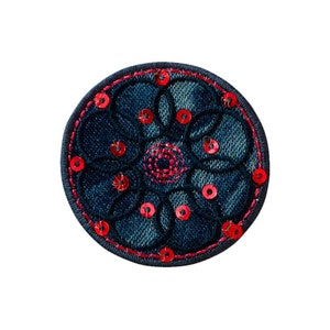 Pode incluir: Um patch circular de ganga com um design floral. O patch apresenta uma base de ganga azul escura com um contorno bordado a vermelho e lantejoulas vermelhas. O centro da flor também é vermelho.