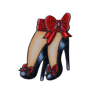 Può includere: Un paio di scarpe nere con tacco alto con fiocchi rossi legati intorno alle caviglie.
