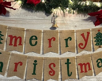 May include: A burlap banner with the words "merry christmas" in red and green letters. Each letter is on a separate flag with a small green Christmas tree on either end of the banner.