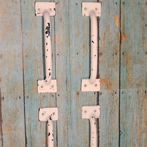 May include: Four white metal door handles with black accents are mounted on a blue and brown wood panel. The handles are slightly distressed, giving them a vintage look.