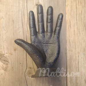 May include: A black cast iron hand sculpture with an open palm. The hand is mounted on a wooden surface.