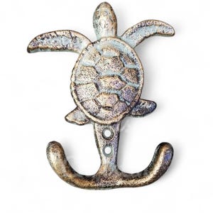 May include: A double hook wall hanger shaped like a sea turtle. The turtle is made of cast iron and has a distressed, antique gold finish with blue and green accents.