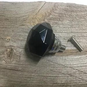 May include: Black glass cabinet knob with a faceted design and a silver metal base. The knob is shown on a wooden surface with a screw.