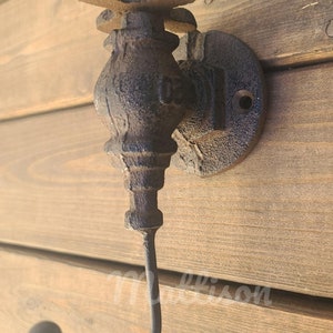 May include: A black cast iron hook shaped like a vintage water faucet with a decorative knob. The hook is mounted on a wooden wall.