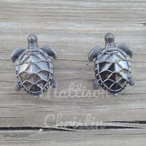 May include: Two black metal turtle drawer pulls. The turtles are facing each other and have a detailed shell design.