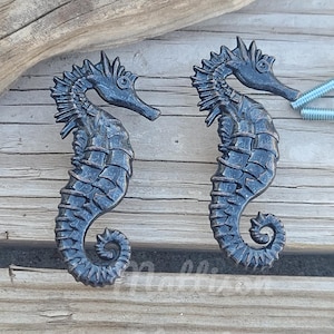 May include: Two black metal seahorse door knobs with a textured finish. The knobs are on a wooden surface.