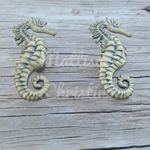 May include: Two gold-toned metal seahorse drawer pulls. The seahorses are facing opposite directions and have a detailed design.