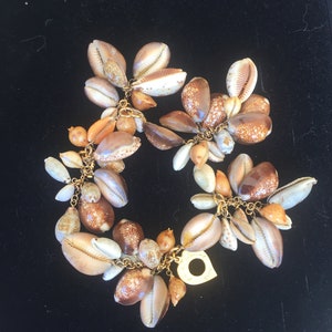 May include: A gold chain bracelet with a heart-shaped charm and many brown, white, and orange seashells attached.