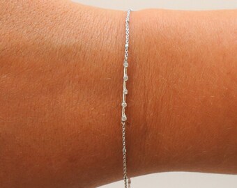 May include: A delicate silver chain bracelet with small round diamonds set in a straight line.