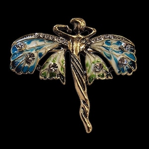 May include: A gold-coloured dragonfly brooch with blue, white, and green enamel wings. The wings are decorated with clear crystals. The dragonfly's body has a stylized figure design.
