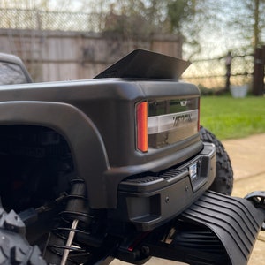 May include: Black pickup truck with a large rear spoiler and black wheels. The truck has a black and silver rear bumper and a black and silver rear tailgate. The truck is sitting on a paved surface.