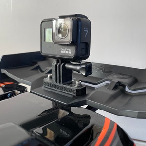 Könnte beinhalten: Eine schwarze GoPro Hero 7 Black Actionkamera, die auf einer schwarzen 3D-gedruckten Halterung montiert ist. Die Halterung ist an einem schwarzen Flügel eines schwarzen und orangefarbenen ferngesteuerten Autos befestigt.
