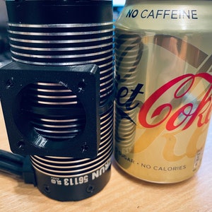 May include: A black and silver electric motor with a cooling fan and the text "56113 SUN" on the side. The motor is next to a can of Diet Coke with the text "NO CAFFEINE SUGAR - NO CALORIES" on the side.
