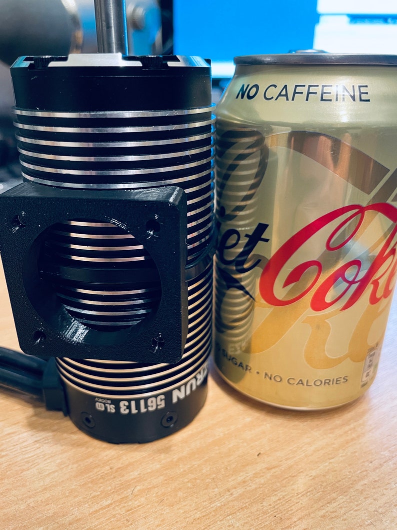 May include: A black and silver electric motor with a cooling fan and the text "56113 SUN" on the side. The motor is next to a can of Diet Coke with the text "NO CAFFEINE SUGAR - NO CALORIES" on the side.