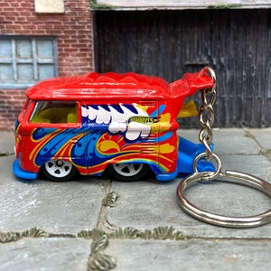 Puede incluir: Llavero Hot Wheels rojo, azul y amarillo con un minibús VW con un diseño colorido. El autobús tiene ruedas blancas y el logotipo de Hot Wheels. Incluye cadena y anillo plateados.
