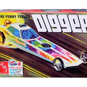 May include: A rectangular model kit box for The Funny Fueler Digger dragster. The box features a colorful illustration of a long, white drag racing car with psychedelic patterns, flames, and the text Digger. The AMT logo and Retro Deluxe label are visible.