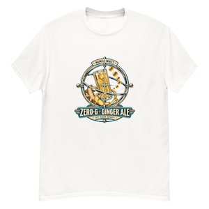 May include: A white t-shirt featuring a graphic of a glass of ginger ale inside a metallic gyroscope ring. The text reads Muncle Mike's ZERO-G GINGER ALE LIFT YOUR SPIRITS. The design includes ginger root and floating bubbles in shades of gold and blue.