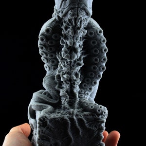 May include: A gray, detailed, 3D printed sculpture of a creature with a human-like head and an octopus-like body. The sculpture is sitting on a square base.