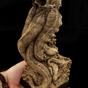 May include: A detailed, bone-colored sculpture of a skull with tentacles, resembling a mythical creature. The sculpture is on a black base and appears to be made of resin.