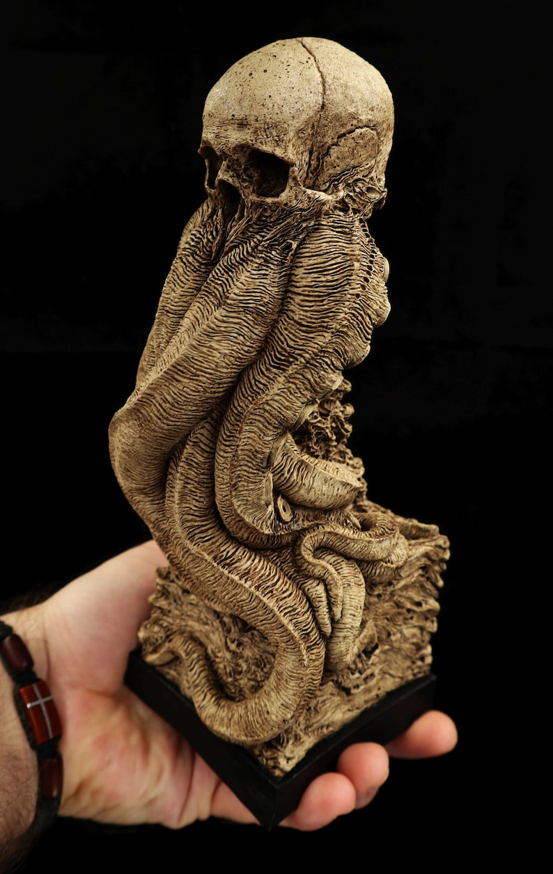 May include: A detailed, bone-colored sculpture of a skull with tentacles, resembling a mythical creature. The sculpture is on a black base and appears to be made of resin.