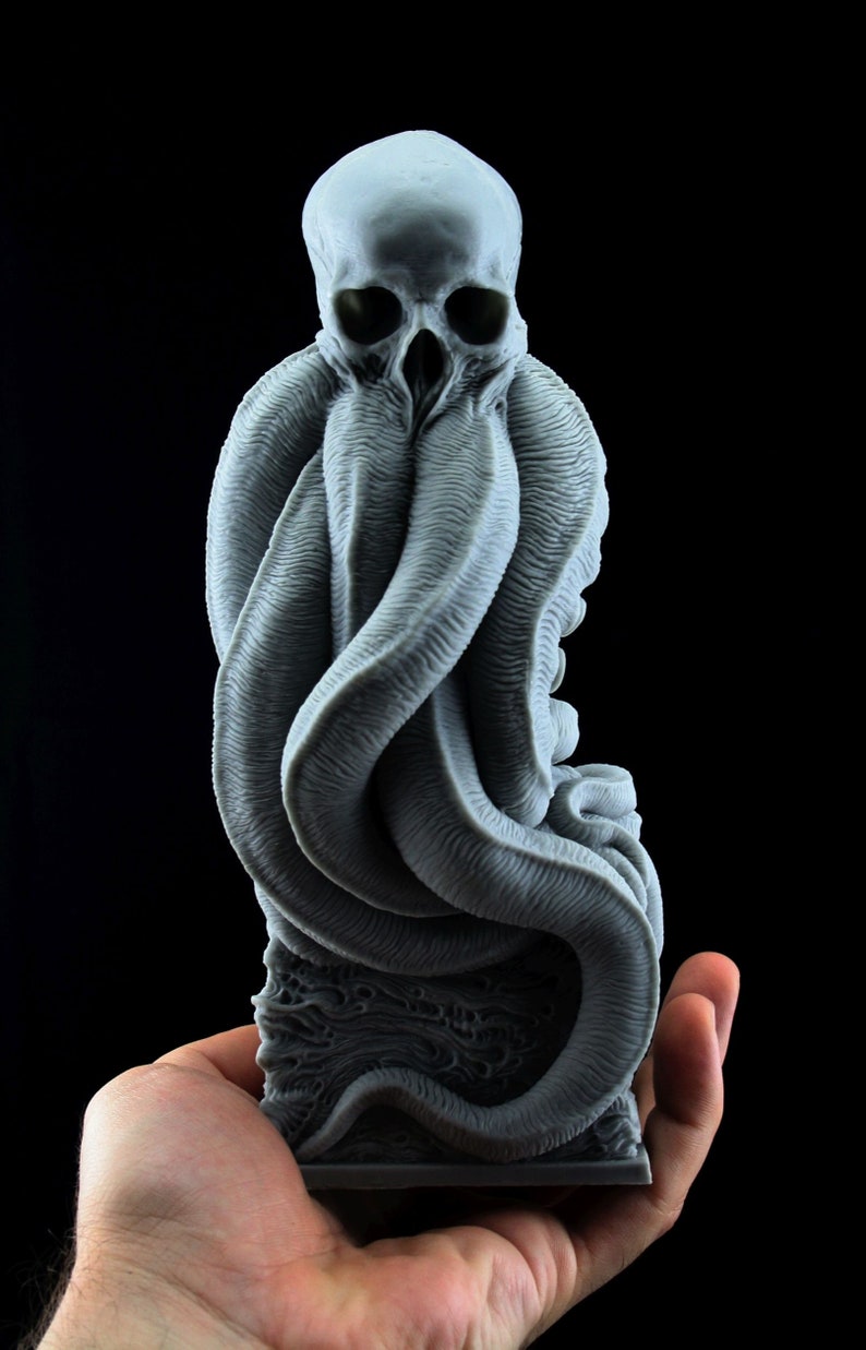 May include: A gray 3D printed sculpture of a creature with a skull-like head and tentacles. The creature is sitting on a base with a textured surface.