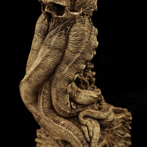 May include: A detailed, skeletal sculpture of a human skull with tentacles, resembling an octopus or squid. The sculpture is made of a light brown material and is set on a dark base.