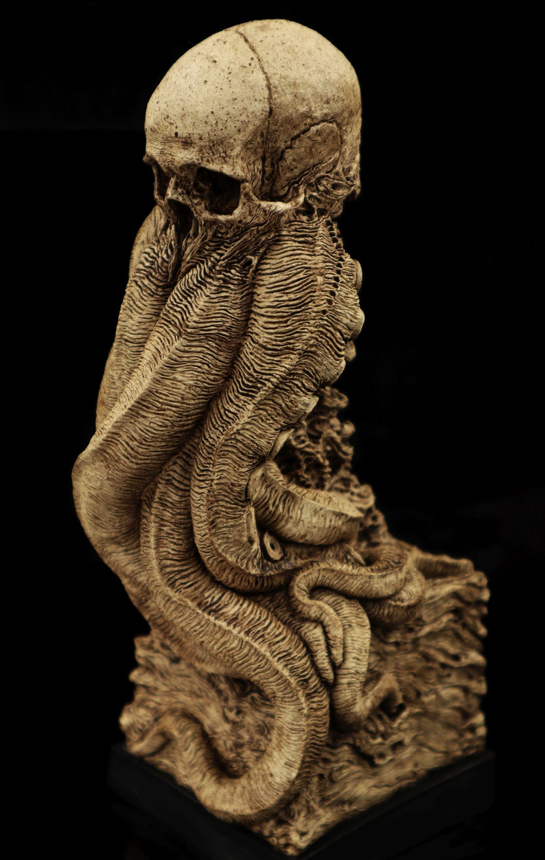 May include: A detailed, skeletal sculpture of a human skull with tentacles, resembling an octopus or squid. The sculpture is made of a light brown material and is set on a dark base.