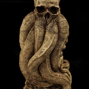 May include: A detailed sculpture of a skull with tentacles wrapped around it. The sculpture is made of a light brown material and has a textured surface.