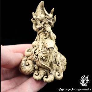 Könnte beinhalten: Eine detaillierte Keramikskulptur einer Kreatur mit einem kronenartigen Kopf und Tentakeln. Die Skulptur ist in einem hellbeigen Farbton bemalt und hat eine strukturierte Oberfläche.