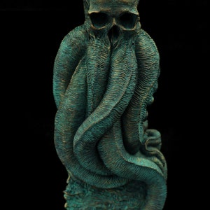 May include: A teal green and gold skull sculpture with tentacles wrapped around it. The sculpture is on a square base.