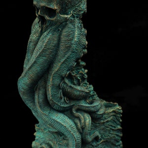 May include: A green and bronze colored sculpture of a skull with tentacles. The skull is on a square base.