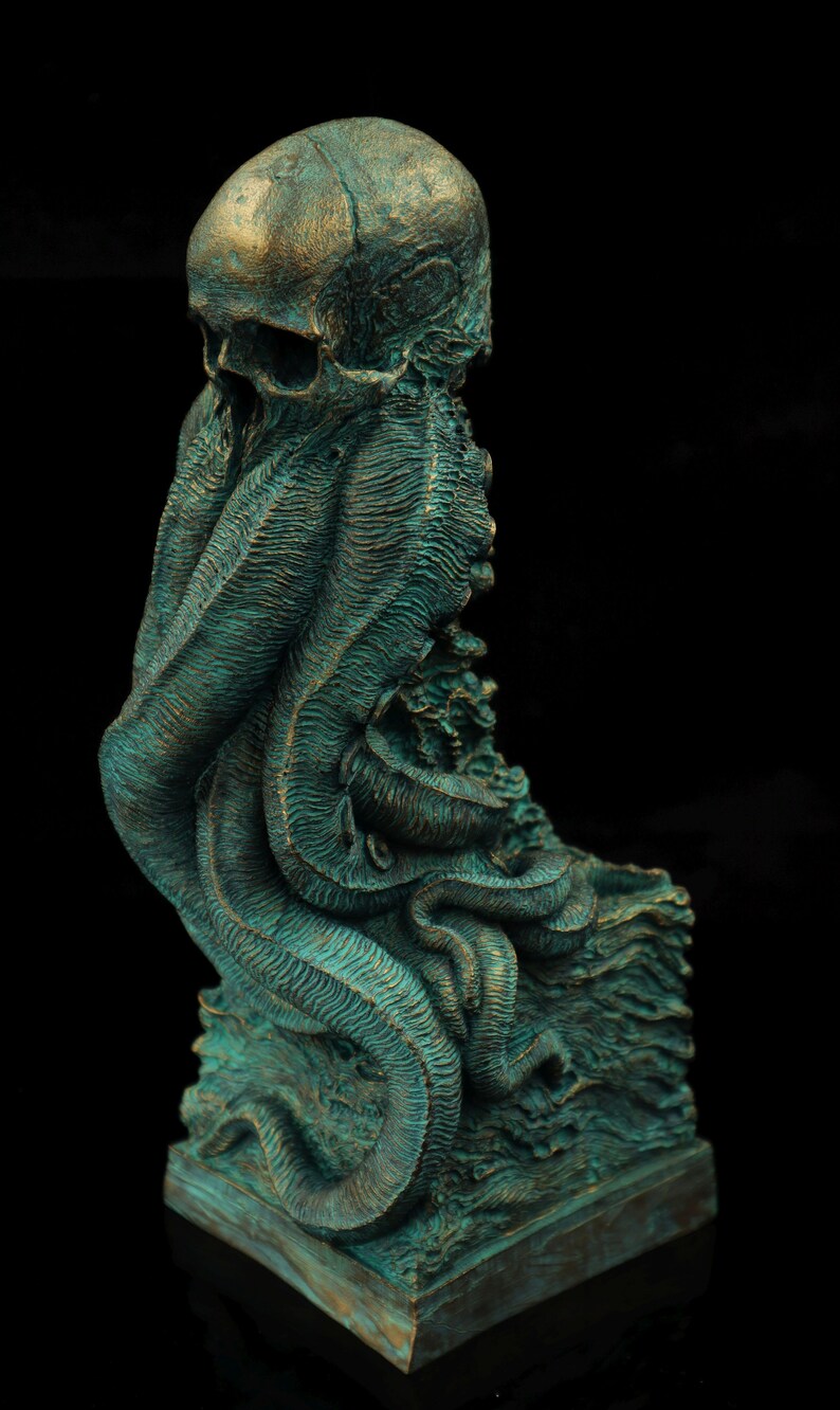 May include: A green and bronze colored sculpture of a skull with tentacles. The skull is on a square base.