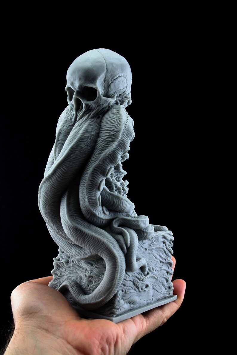 May include: A gray 3D printed sculpture of a skull with tentacles emerging from its head. The sculpture is on a base that resembles a rocky surface.