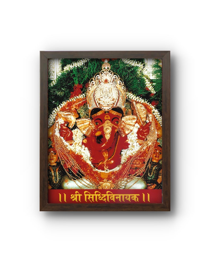 May include: Framed image of a red deity with a golden crown and jewelry, surrounded by garlands and greenery. The image has text in a foreign language at the bottom and is set in a dark brown frame.