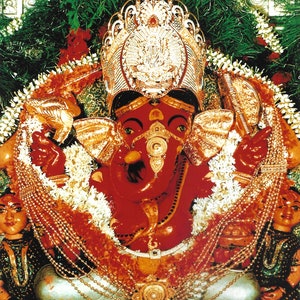 May include: A vibrant image of a red-skinned deity, adorned with gold jewelry and a jeweled crown. The deity is surrounded by garlands of flowers and greenery. The text at the bottom reads in a foreign language.