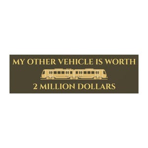 以下が含まれることがあります： MY OTHER VEHICLE IS WORTH 2 MILLION DOLLARSという金色の文字が書かれた濃い茶色の長方形のステッカー。2行のテキストの中央には、金色の旅客列車のグラフィックが配置されています。