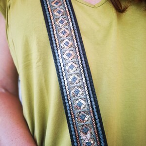 May include: A black guitar strap with a blue and gold geometric pattern. The strap is decorated with sequins and has a silver buckle.